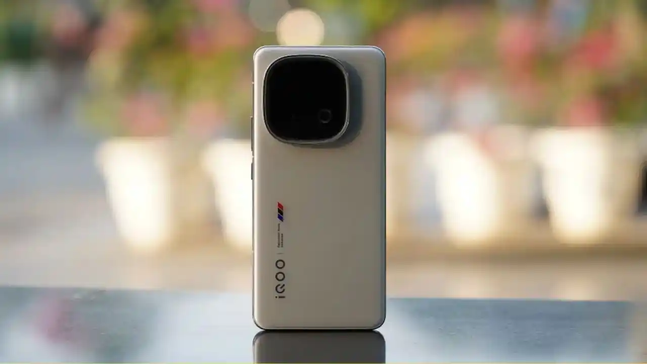 Futuristic promotional render of the iQOO 15, showcasing its premium metallic finish, edge-to-edge 2K OLED display, and rear camera module, set against a dynamic blue-orange tech background with launch announcement.
